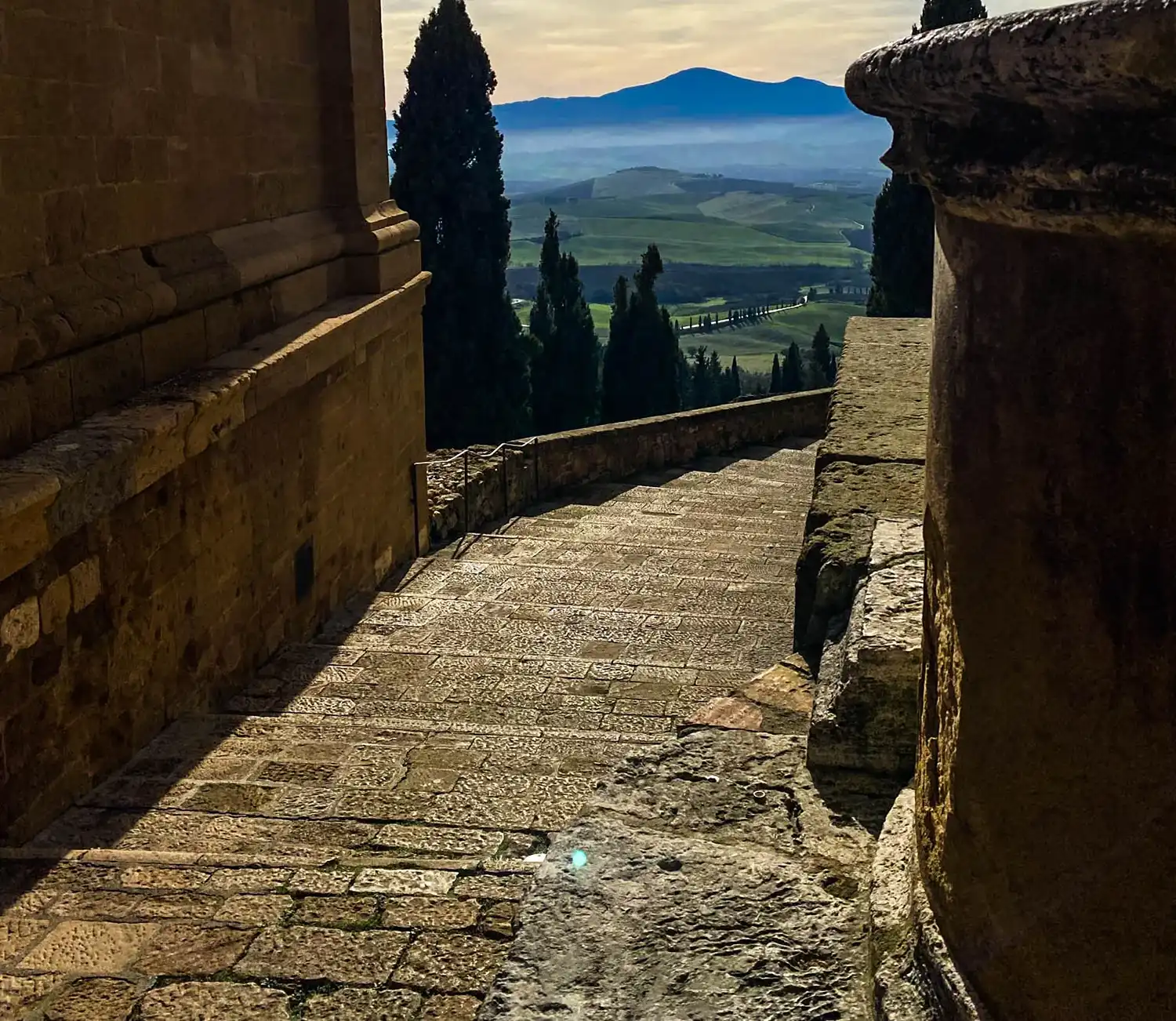 a stone walkway with a stone column and a mountain in the distance